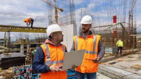 Male Caucasian building contractors, investors, architects, or engineers, planning and supervising work at the construction site, while using a laptop and digital tablet